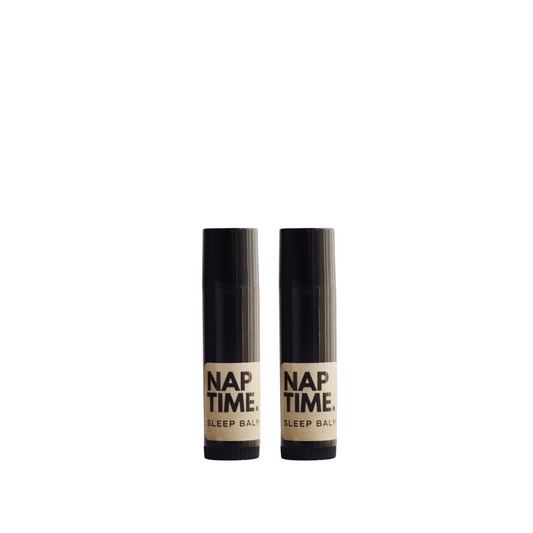 The image displays two identical cylindrical tubes of a product labelled “Nap Time Sleep Balm.” The tubes sleek design each with a black body and cap which gives the product a modern and unisex appeal. The label on each bottle has a minimalist design with a beige background and black lettering, clearly stating the product name and its designation as a sleep balm. 