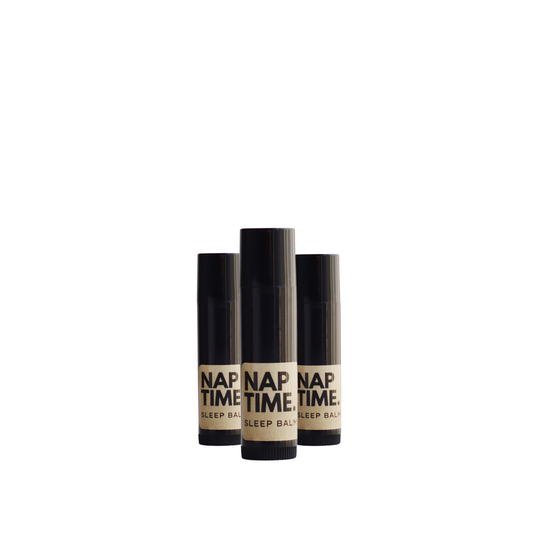 The image displays three identical cylindrical tubes of a product labelled “Nap Time Sleep Balm.” The tubes sleek design each with a black body and cap which gives the product a modern and unisex appeal. The label on each bottle has a minimalist design with a beige background and black lettering, clearly stating the product name and its designation as a sleep balm. and sleep aid.