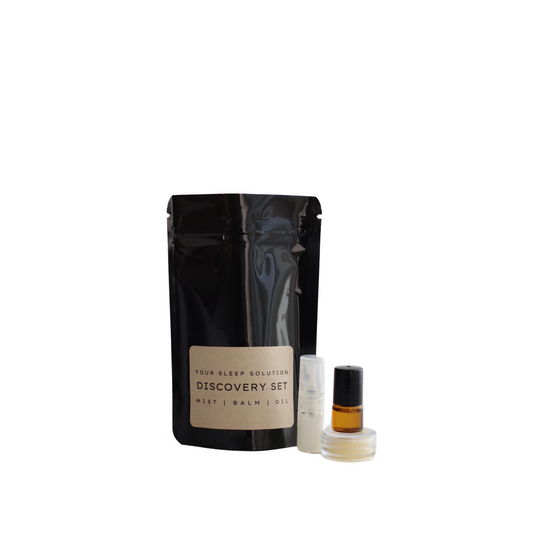 Nap Time the all natural Australian sleep solution discovery kit. The kit includes a mist, a balm, and an oil designed to connect your mind and body with sleep. On the left is a tall, slender black pouch with a beige label. To the right, there are three small containers: a clear bottle with a white liquid, a similar bottle with a dark amber liquid, and a small jar with a creamy balm. The background is plain white, emphasizing the simplicity and clean design of the products.