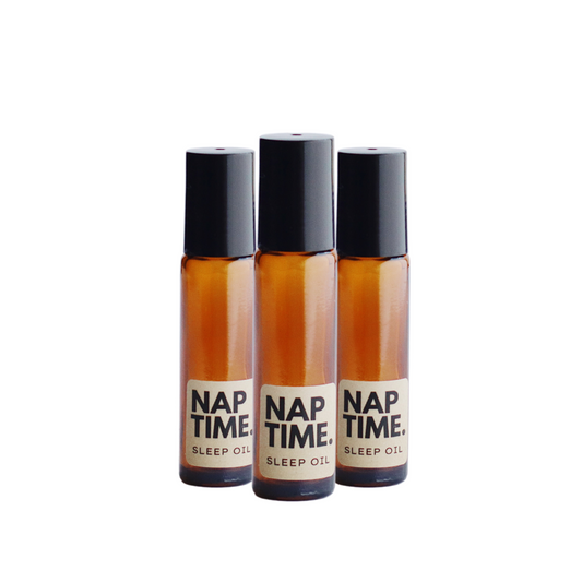 The image displays three identical bottles of a product labelled “Nap Time Sleep Oil.” The bottles have a simple clean design with transparent Amber Glass and black caps. The labels are minimalist with beige background and black text clearly indicating the product name and its purpose. The oil inside appears to be golden colour visible through the glass, which suggests a natural ingredient commonly associated with sleep aids or relaxation products.